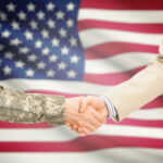 serviceperson shaking hands in front of U.S. flag