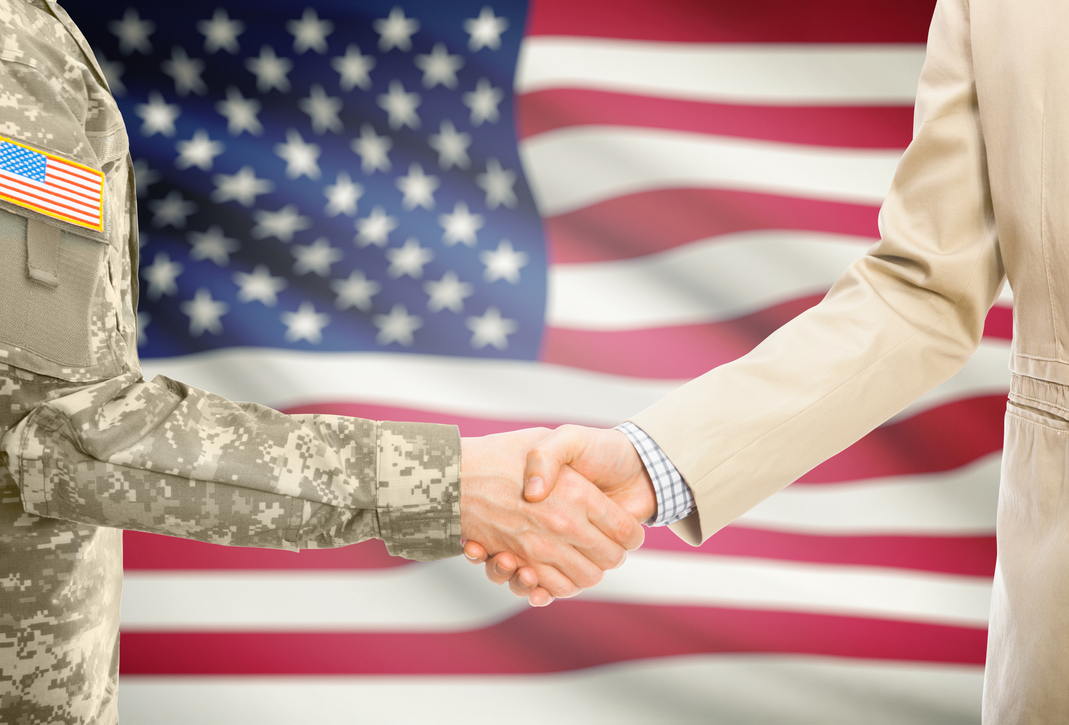 serviceperson shaking hands in front of U.S. flag