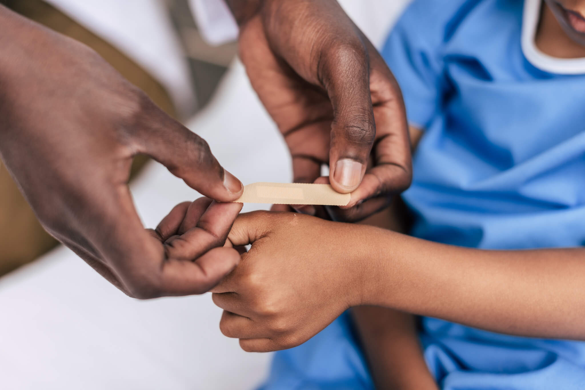 close-up of hands of adult putting band aid on child's hand