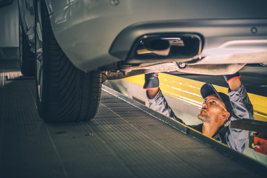 man inspecting standing and inspecting the undercarriage of car in a service dock