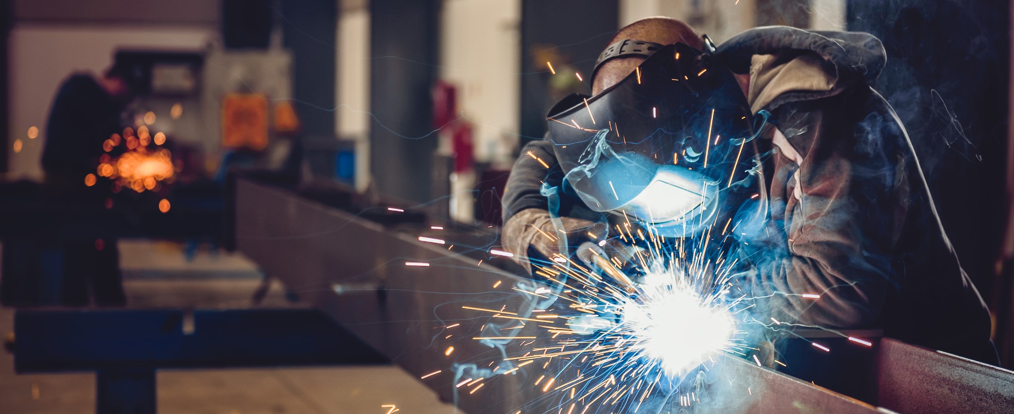 Industrial Welder With Torch and Protective Helmet in big hall welding metal profiles